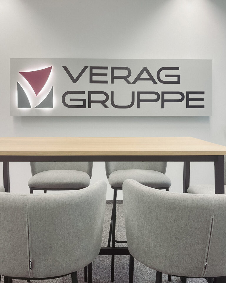 Aufnahme eines Meetingtisches, dahinter das Unternehmenslogo an der Wand
